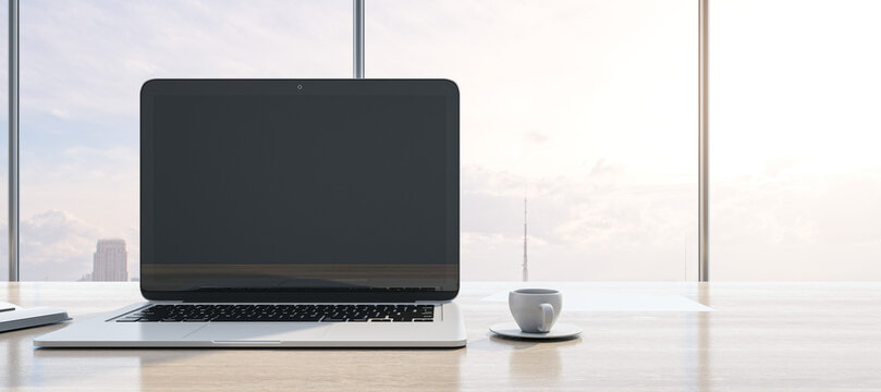 Close up of modern workspace with empty mock up laptop screen, supplies, coffee cup and panoramic window with city view in the background. 3D Rendering.