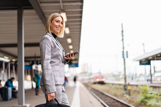Smiling young businesswoman with mobile phone at the train station