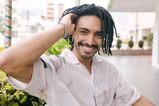 Happy young man with hand in hair sitting near plants