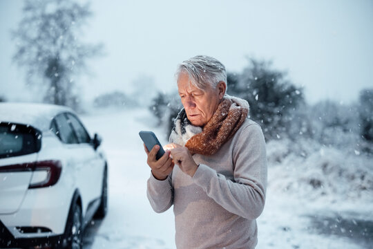 Senior man using smart phone near car in snow