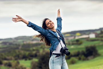Carefree young woman standing with arms raised under sky
