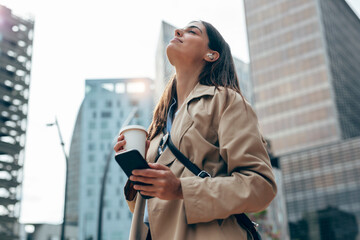 Young woman with eyes closed holding coffee cup and smart phone in city