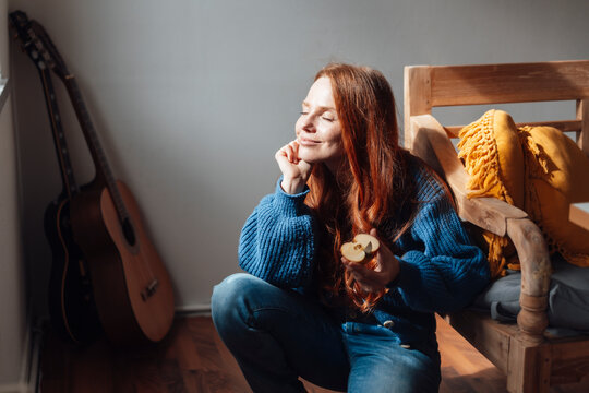 Smiling redhead woman crouching with slice of apple at home