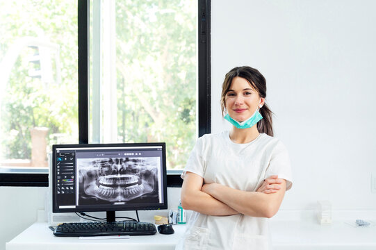 Smiling dentist with arms crossed standing near x-ray Image on computer screen
