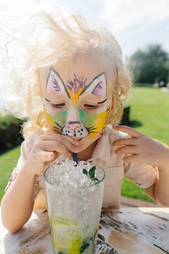 Girl with face painting drinking mojito in garden