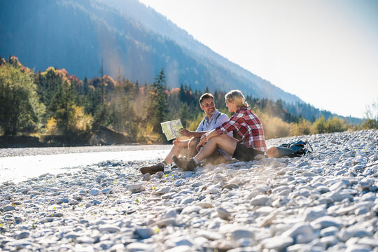 Austria, Alps, couple on a hiking trip having a break at a brook reading map