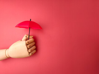 Wooden hand holding red umbrella on a red background with copy space. - obrazy, fototapety, plakaty