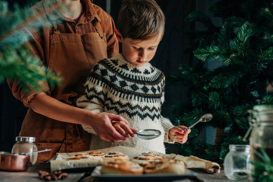 Mother and son dusting sugar on cinnamon buns at table