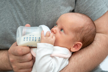 New father's experience, man holding his baby, offering formula milk with care