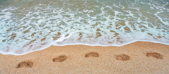 Sea waves wash away footprints on the sandy beach at the water's edge. The concept of summer holidays, walks along the coast.