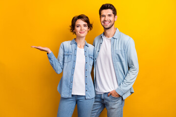 Photo of cute sweet positive couple wear stylish denim clothes presenting empty space black friday offer isolated yellow color background