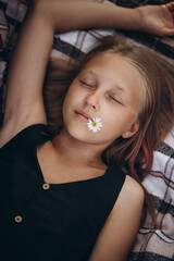 girl lies with her eyes closed and holds a chamomile in her mouth