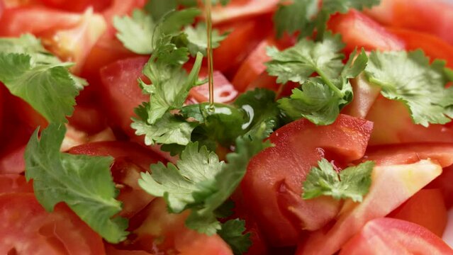 Pouring olive oil on a fresh cooking salad with tomatoes and cilantro herbs close up. Rotation