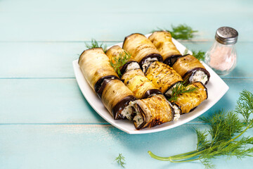 Appetizer of eggplant with cream cheese on a white plate. Keto appetizer of baked eggplant on a blue wooden background. Keto diet. Top view.