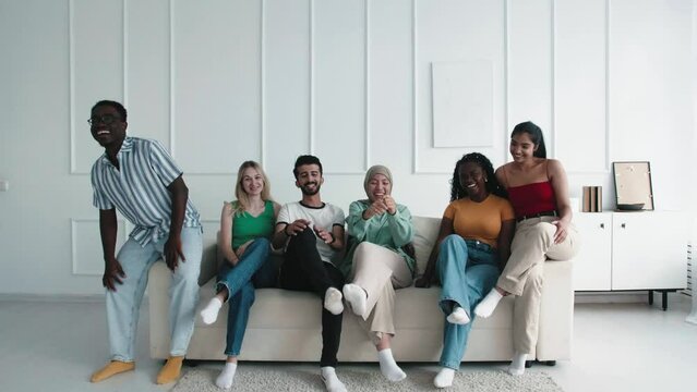Happy group of young friends smiling at camera. Portrait of joyful cheerful multiracial student people having fun together coming and sitting on the sofa. multicultural diverse young Friends laughing.