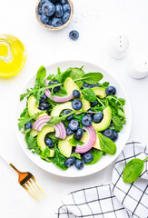 Gourmet vegan salad with blueberry, avocado, red onion, spinach, arugula and mixed herbs, white table background, top view