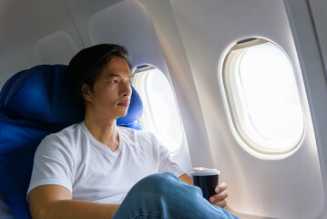 Asian man airplane passenger with coffee cup looking at plane window, man traveler in casual wear...