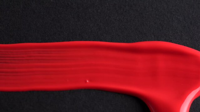 Close-up of artist holding paint brush and drawing oil painting. Painting red line on black paper.
