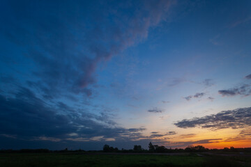 Naklejka na ściany i meble View of evening clouds and sky after sunset over a meadow