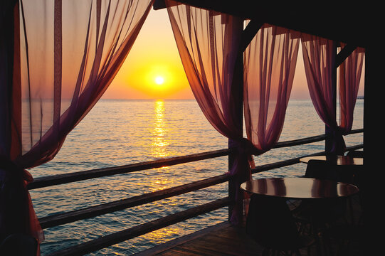 A beautiful image of a sunset over a calm sea from the curtains of a restaurant on the beach.