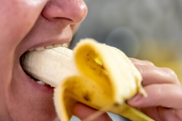 An adult woman eats a banana, close-up.