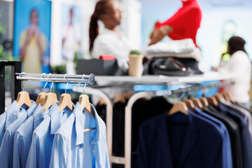 Formal shirts and jackets hanging on display rack showcasing latest arrival merchandise in retail shopping mall with blurred background. Apparel on hangers in fashion boutique close up
