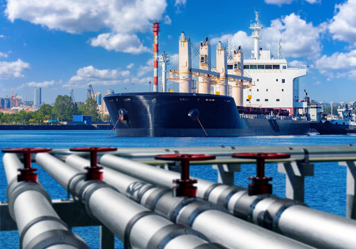 Fuel terminal at port. Ship sails into harbor. Pipes for refueling marine vessel. Oil loading station in port. Pipeline with oil near ocean. Ship near cargo port. Oil sea terminal on summer day