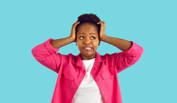 Funny woman who made mistake or forgot something grabs her head on light blue background. Portrait of African American woman looking to side with guilty expression on her face. Web banner.