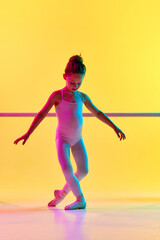 Portrait of small delicate child ballerina dancer girl on pointe shoes posing near barre in mixed neon light. Kinds personality development concept.
