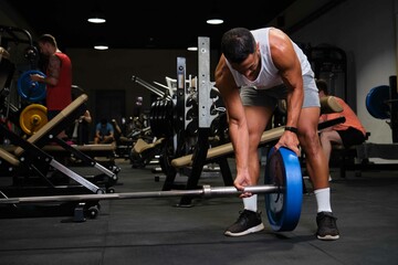 Fototapeta na wymiar Strong Hispanic man removing weight plate on barbell after deadlift at a gym.