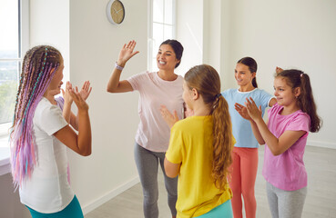 Female friendly choreographer giving high five to her happy smiling kids students girls in choreography studio after doing dance workout. Children sport and active lifestyle concept.