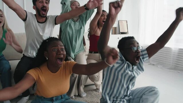Multiracial excited friends watching football in streaming at home. Football fans watching game and celebrating victory score in the living room. Happy supporters cheering