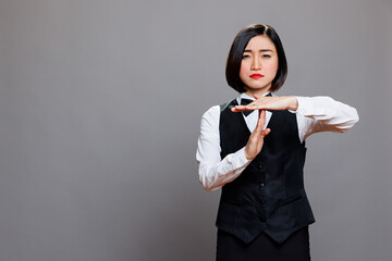 Confident asian waitress wearing uniform showing timeout sign with arms portrait. Restaurant serious woman employee asking to take break while making gesture with hands and looking at camera - obrazy, fototapety, plakaty