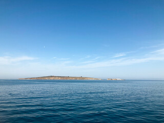 Island in a calm sea. View from the ship. Clear sunny day - 652234155