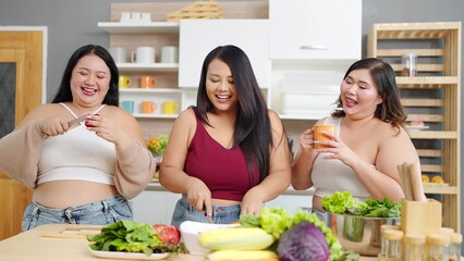 Group of cheerful chubby women friends cooking, preparing salad together. Three Asian plus size women talking and cooking salad in kitchen room. Healthy food concept