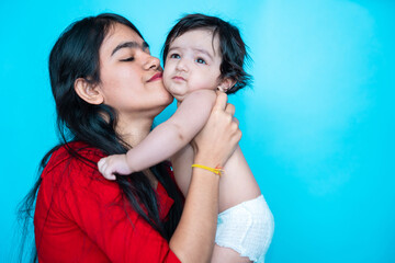 Indian teenager girl playing six months cute little baby in diaper isolated over blue background. Asian infant child and sister, Happy family. - obrazy, fototapety, plakaty