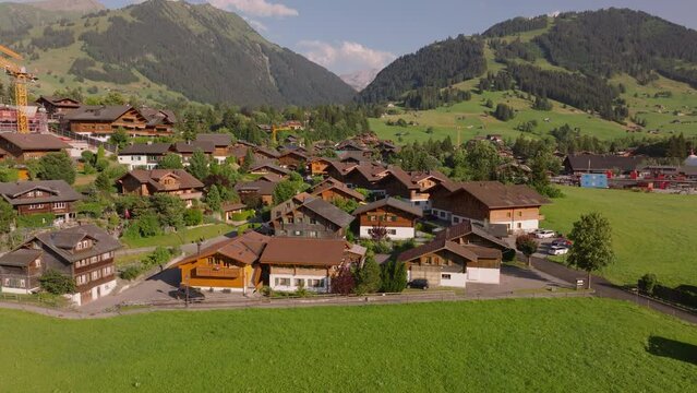 Wooden houses in traditional alpine town on sunny day. Aerial view of buildings with mountains in background. Gstaad, Switzerland