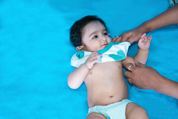 Indian mother changing cloths of cute six months old baby boy wearing diaper lying on floor...