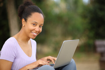 Black woman looks at you using laptop in a park