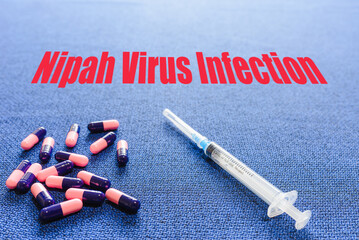 Nipah virus concept.A blue background with the inscription NIPAH VIRUS INFECTION.Top view, syringe tablets pills lying on the table.Nipah virus healthcare concept.
