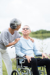 Happy Life Retirement, Asian Elderly wife take care husband sitting on wheelchair in the park...