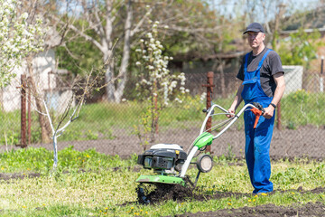 Farmer man plows the land with a cultivator preparing the soil for sowing