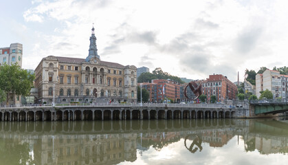 Panorama exterior view at the iconic Bilbao City Hall, Bilbao downtown city, Nervion river and river banks and buildings - obrazy, fototapety, plakaty