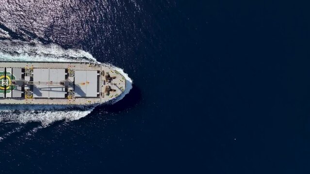 Aerial top down view a large general bulk cargo ship traveling with speed over blue ocean