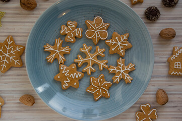 Painted traditional Christmas gingerbreads arranged on blue plate on white wooden table, various xmas shapes