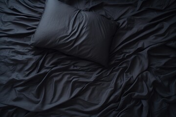 Top view of an unmade black bed with a crumpled sheet, blanket and pillows - Powered by Adobe