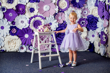 Obraz na płótnie Canvas A girl in a light purple dress with a festive cake on a floral white-purple background. Birthday photoshoot.