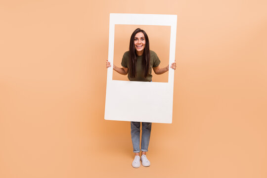 Full length photo of excited charming girl dressed khaki t-shirt tacking photo paper frame isolated beige color background