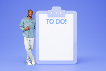 Smiling millennial african american man in casual point finger on plan to do with copy space