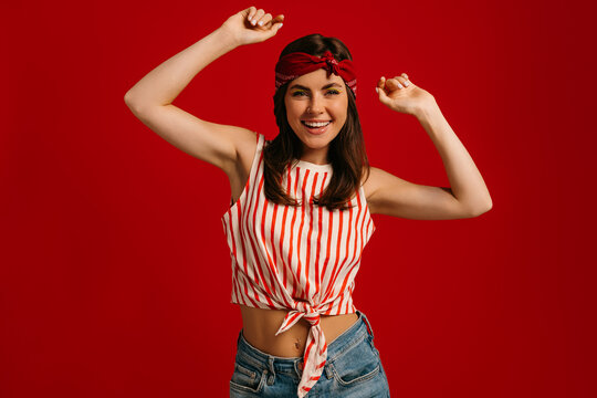 Stylish young hipster woman dancing and smiling while standing on red background